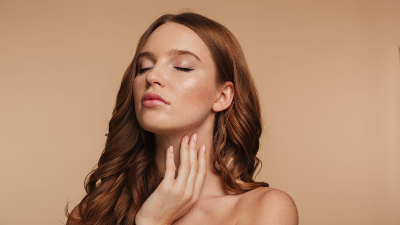Beauty portrait of sensual ginger woman with long hair posing with closed eyes over cream background