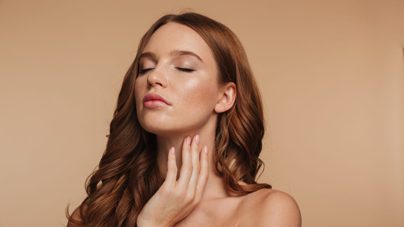 Beauty portrait of sensual ginger woman with long hair posing with closed eyes over cream background